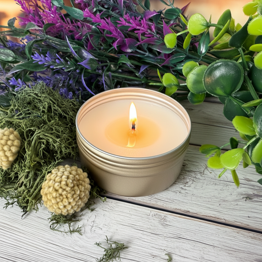 2oz travel tin candle (lit) in a gold tin, small flame glow with greenery and rustic props.