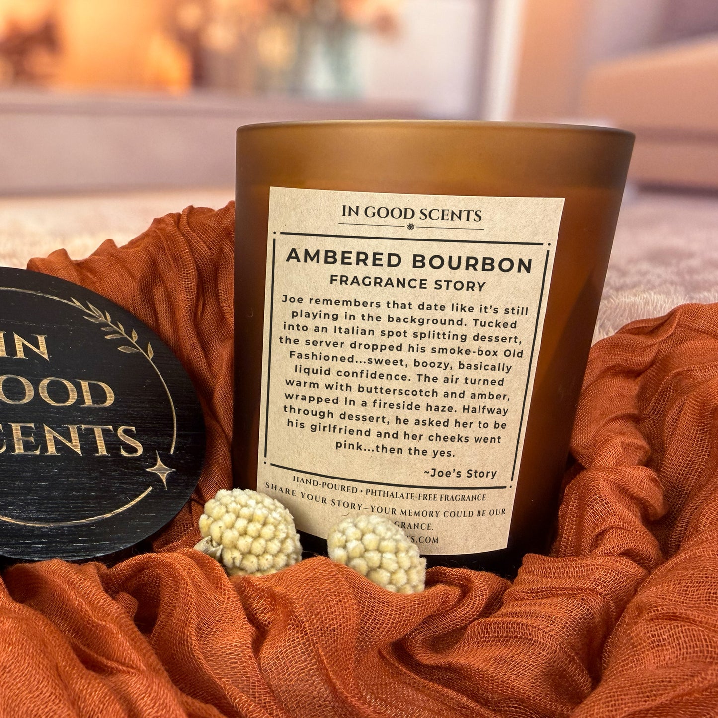 Ambered Bourbon fragrance story label on 12oz amber jar candle styled on rust fabric with black In Good Scents lid.