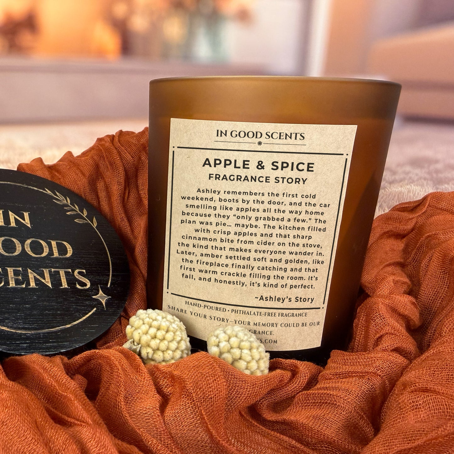 Apple & Spice fragrance story label — In Good Scents 12oz amber candle with “Fragrance Story” label, styled on warm rust fabric with branded lid nearby.