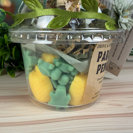 Clear container with yellow and green wax melts, including a plant, on a wooden surface.