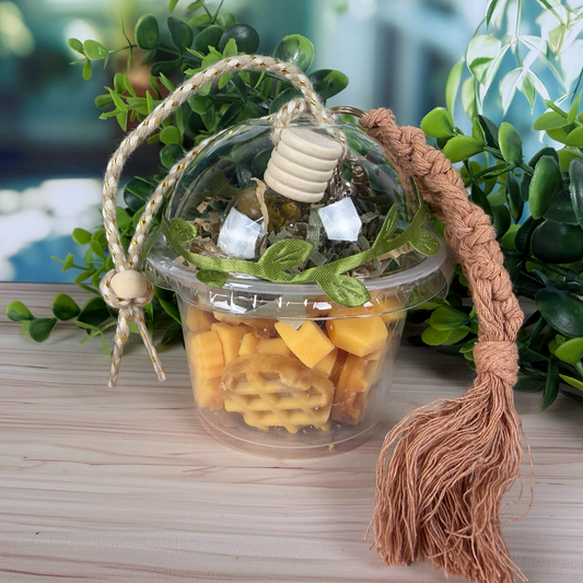 Decorative container with plant, glass diffuser, and tassel on a wooden surface with greenery in the background.