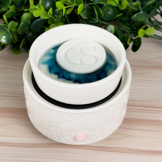 White wax warmer with blue melted wax and a round GS logo wax melt on top.