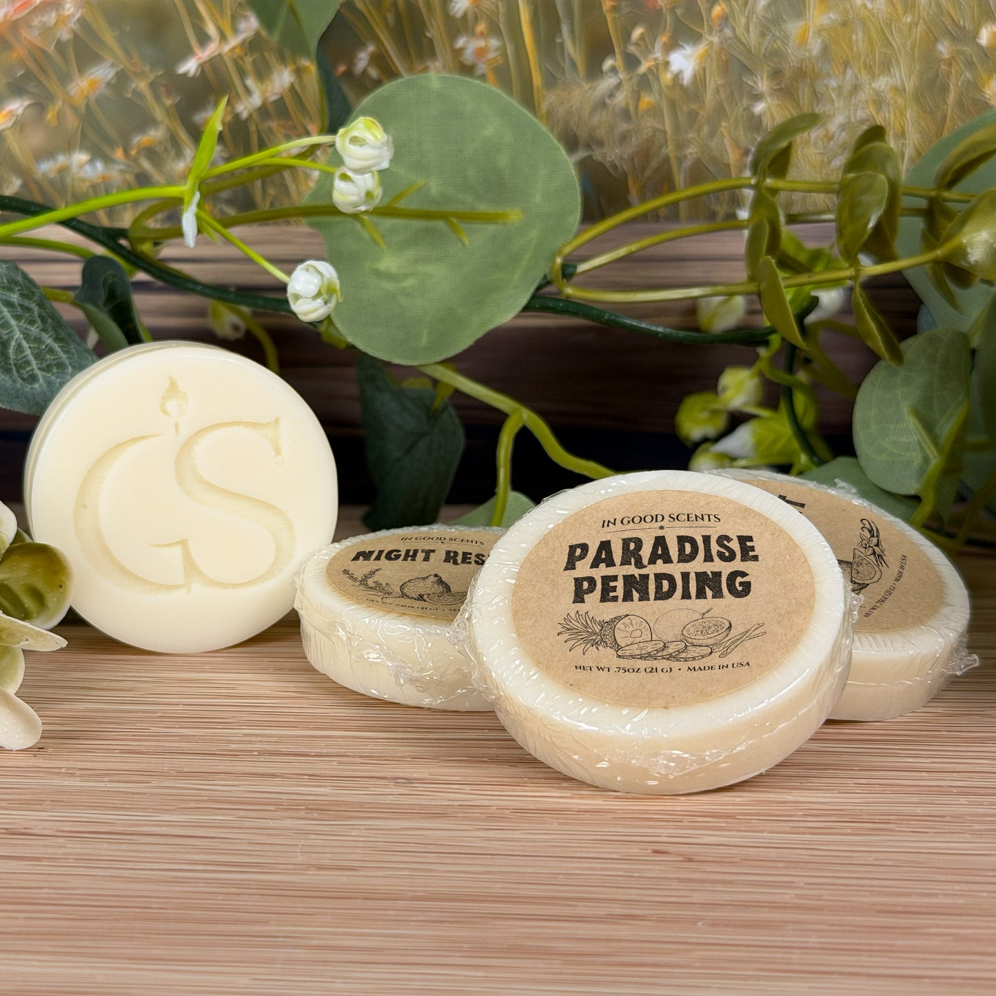 Paradise Pending wax melt tart with GS logo alongside other In Good Scents melts in a styled floral setup.