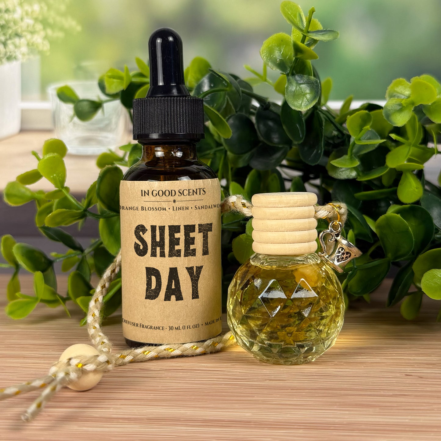 Two small diffuser bottles with labels on a wooden surface with greenery in the background