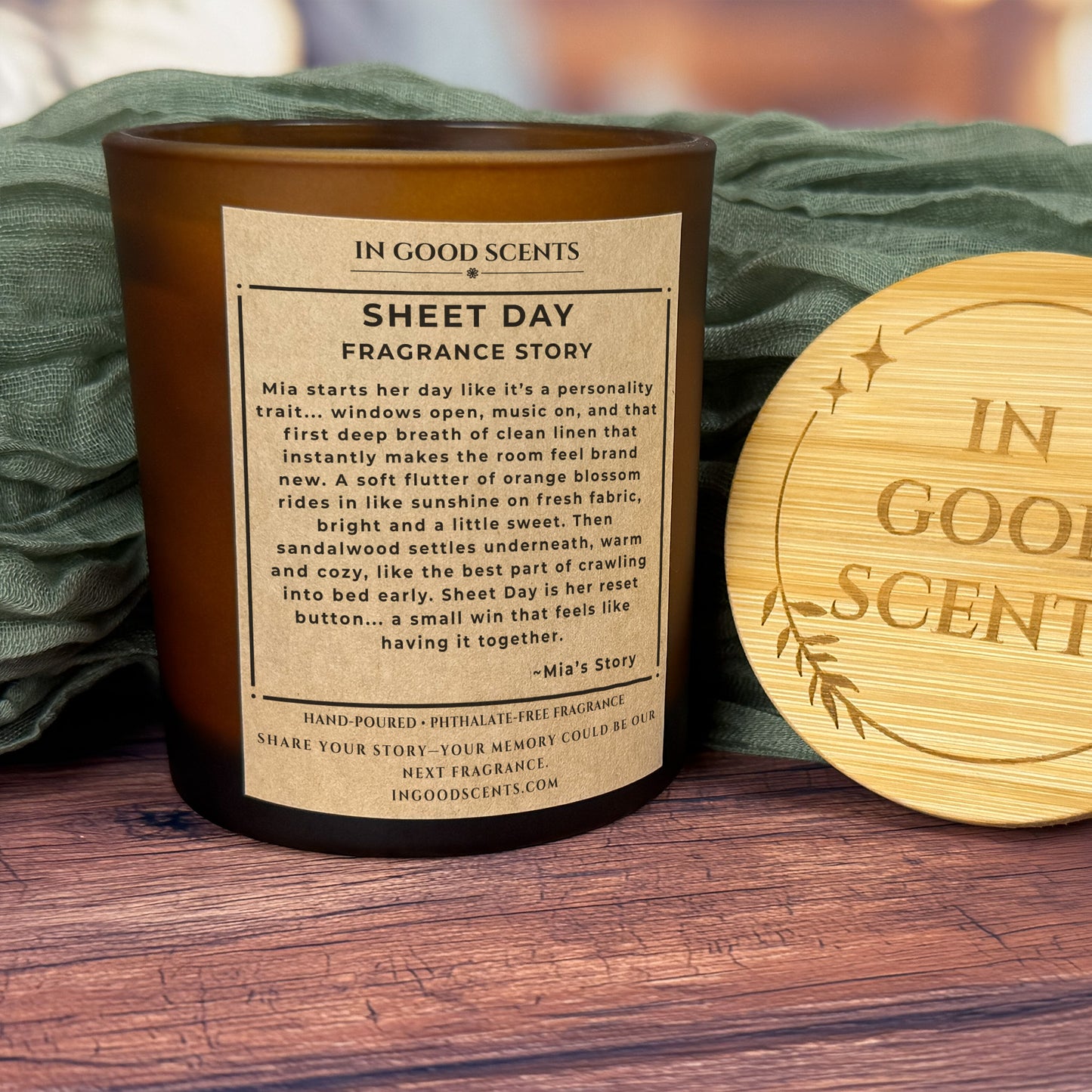 Back label view (Fragrance Story) of Sheet Day 8oz candle in an amber jar, styled with green fabric and bamboo lid on a wood surface.