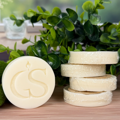 After Hours wax melt tart (0.75 oz) with kraft label, shown stacked with an embossed “GS” tart on a whitewashed wood surface with purple florals and moss.