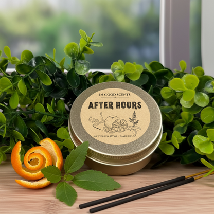 After Hours 2oz tin candle by In Good Scents, top view with “After Hours” label, styled with greenery, orange peel, and incense sticks on a wood surface.