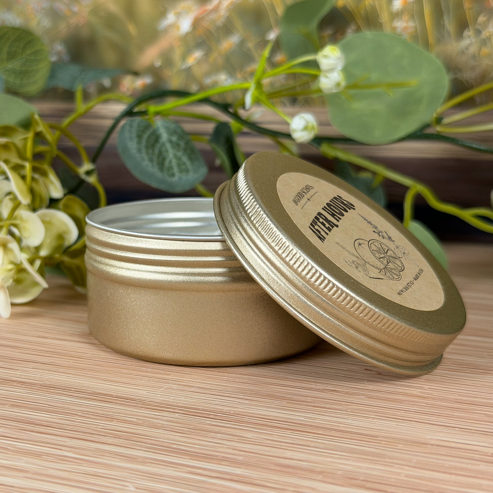 After Hours 2oz tin candle by In Good Scents, open tin with lid resting beside it, label visible, styled with soft greenery on a wood surface.
