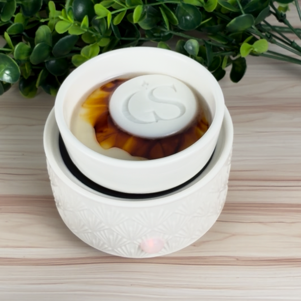 White electric wax warmer melting an Ambered Bourbon wax tart, topped with a GS logo wax embed.