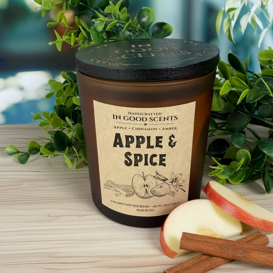 Apple & Spice 12oz candle with lid — In Good Scents amber glass jar on light wood surface with fresh apple slices and cinnamon sticks.