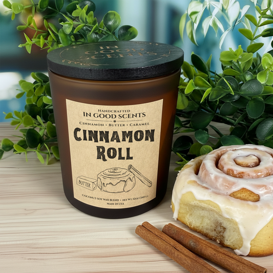 Cinnamon Roll 12oz amber jar candle with black lid, styled with cinnamon roll and cinnamon sticks on wood surface