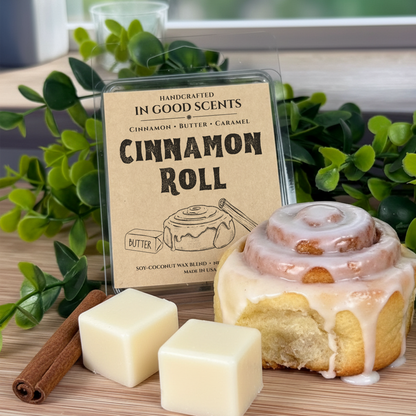 Cinnamon roll-themed wax melt with packaging labeled 'Cinnamon Roll' on a wooden surface with greenery.