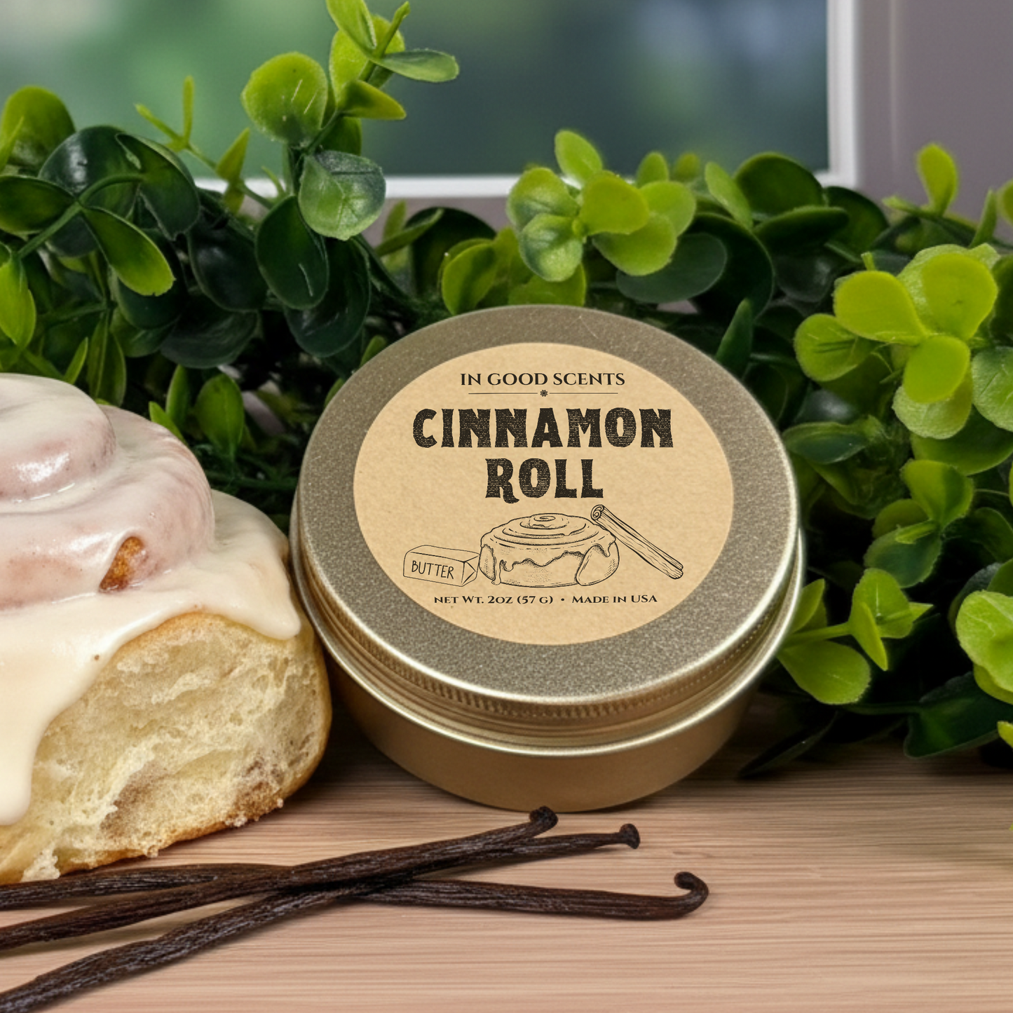 In Good Scents “Cinnamon Roll” 2oz travel tin candle on wood surface with iced cinnamon roll and vanilla beans.