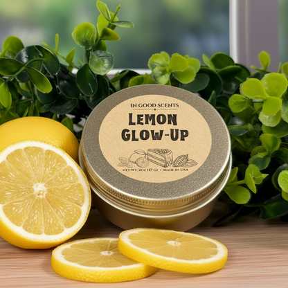 In Good Scents “Lemon Glow-Up” 2oz travel tin candle with sliced lemons on wood surface and greenery backdrop.