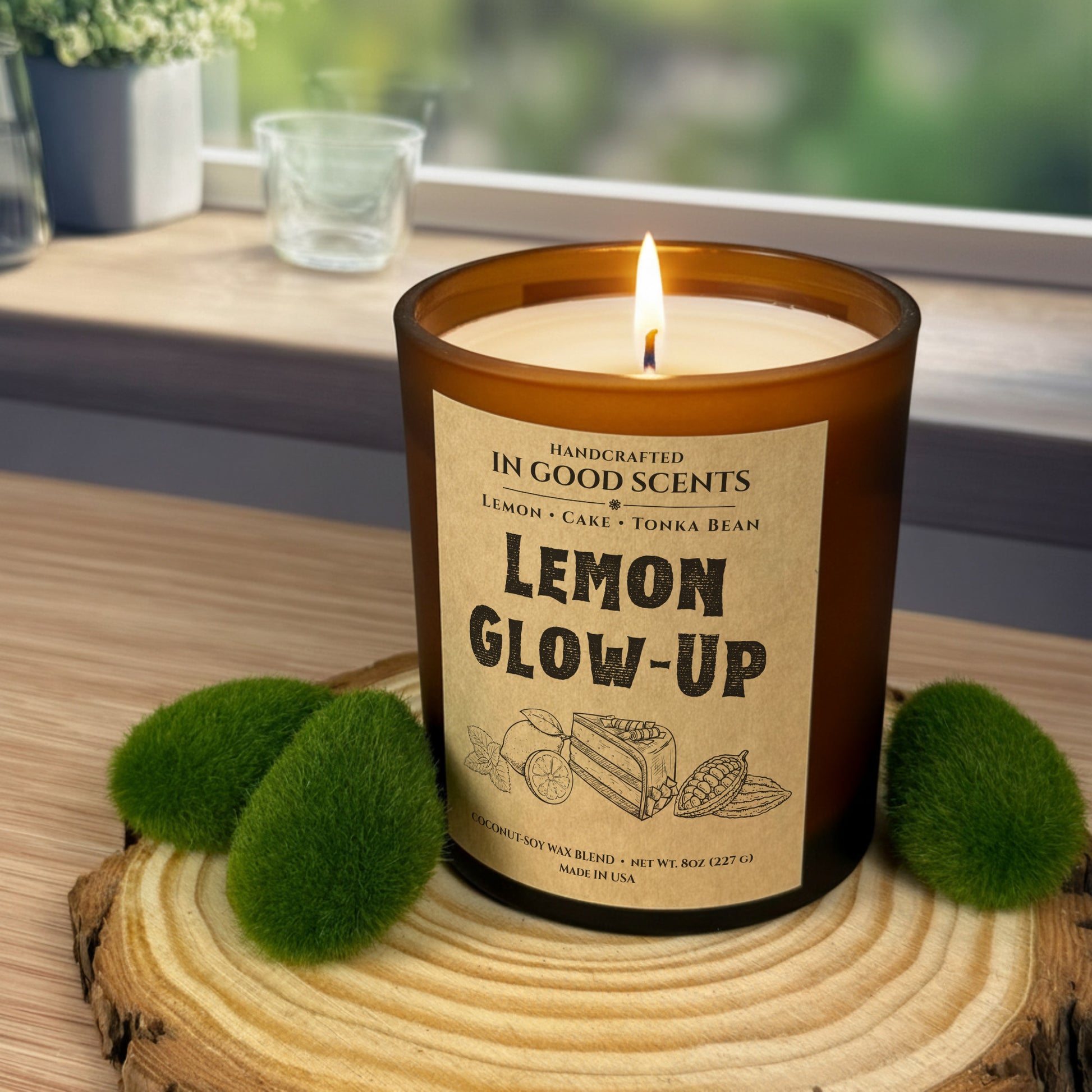 Lit Lemon Glow-Up 8oz candle in amber jar on a wood slice with green moss decor, bright window background.