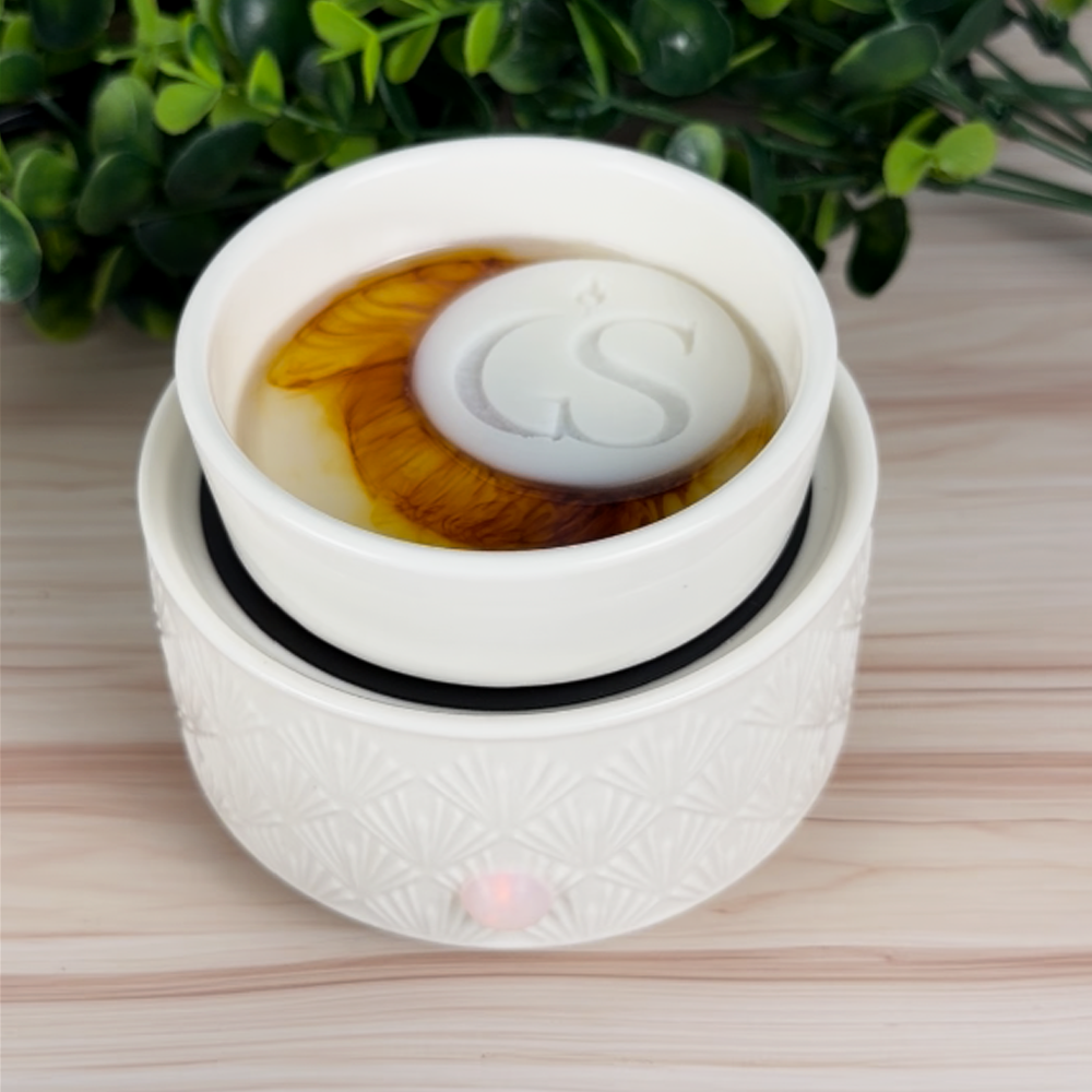 Morning Ritual wax melt tart melting in white wax warmer dish, showing orange brown-toned color swirl and GS logo melt on top.