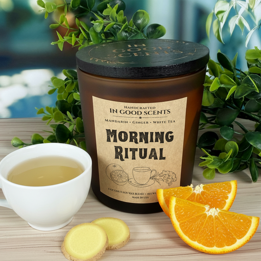 Morning Ritual 12oz candle with tea cup, ginger slices, and orange wedges on light wood background