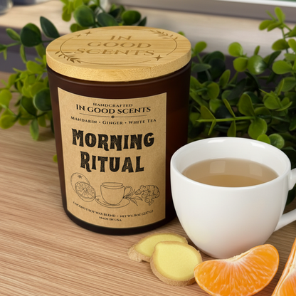 Morning Ritual 8oz amber jar candle with bamboo lid on wood tabletop, green plants in background.
