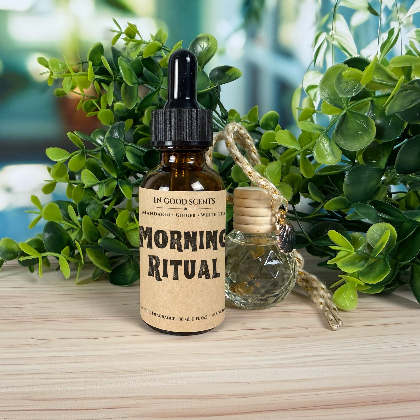 Morning Ritual diffuser fragrance oil bottle (dropper top) beside the matching hanging car diffuser with braided cord, styled with greenery on a light wood surface.