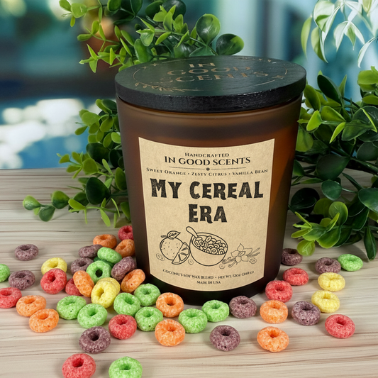 In Good Scents “My Cereal Era” 12oz amber jar candle with black lid, surrounded by colorful cereal loops on a wooden surface.