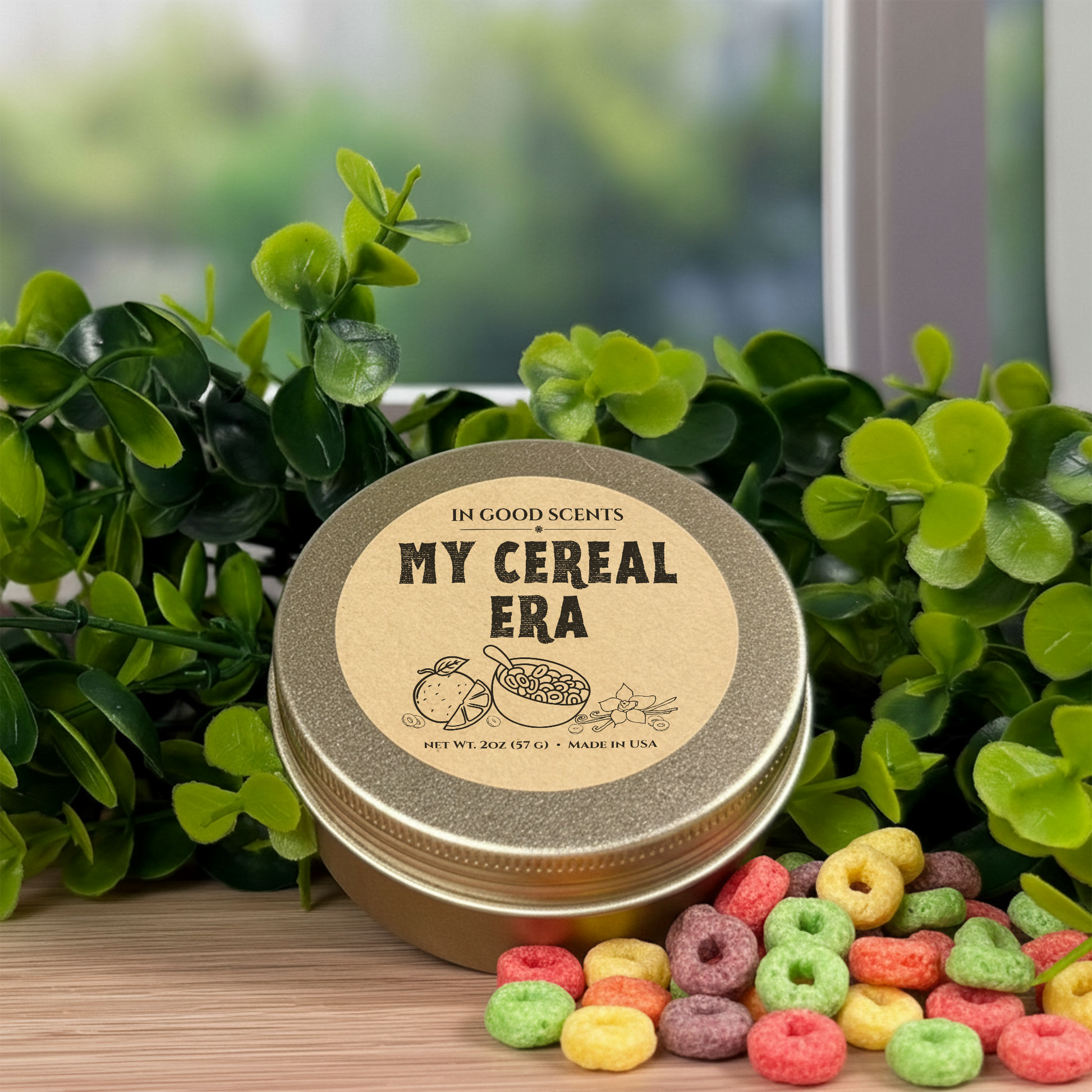 My Cereal Era 2oz Travel Tin Candle (In Good Scents) on a wood surface with green foliage and colorful cereal pieces, label shown on lid.