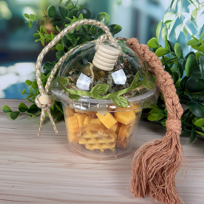 Decorative container with plant, glass diffuser, and tassel on a wooden surface with greenery in the background.