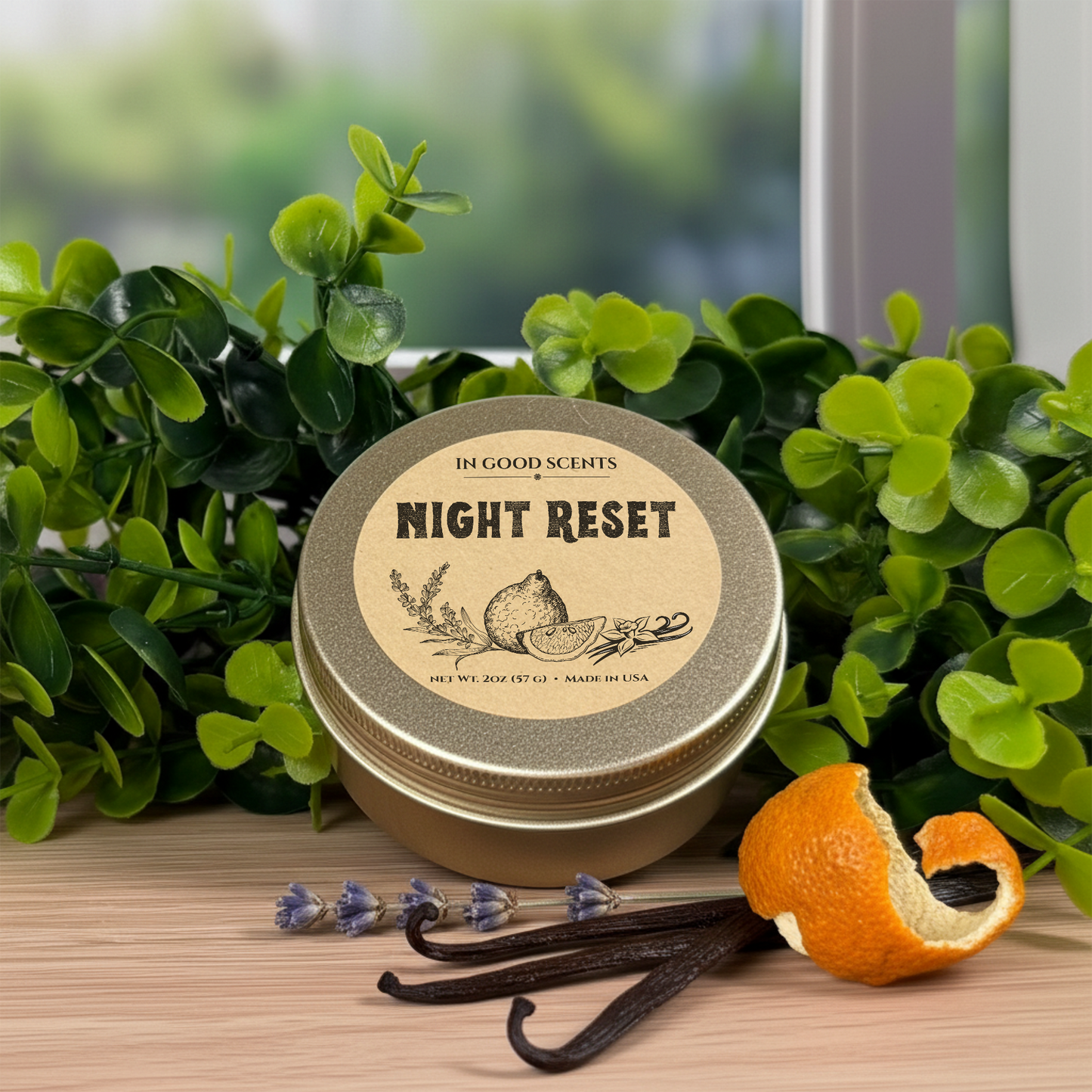 Night Reset 2oz Travel Tin Candle (In Good Scents) on a wood surface with green foliage, orange peel, lavender, and vanilla beans.