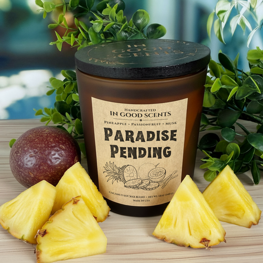 In Good Scents ‘Paradise Pending’ 12oz amber jar candle with black lid, styled with pineapple slices and passionfruit.