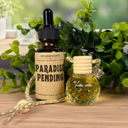 Two small bottles with labels on a wooden surface with greenery in the background