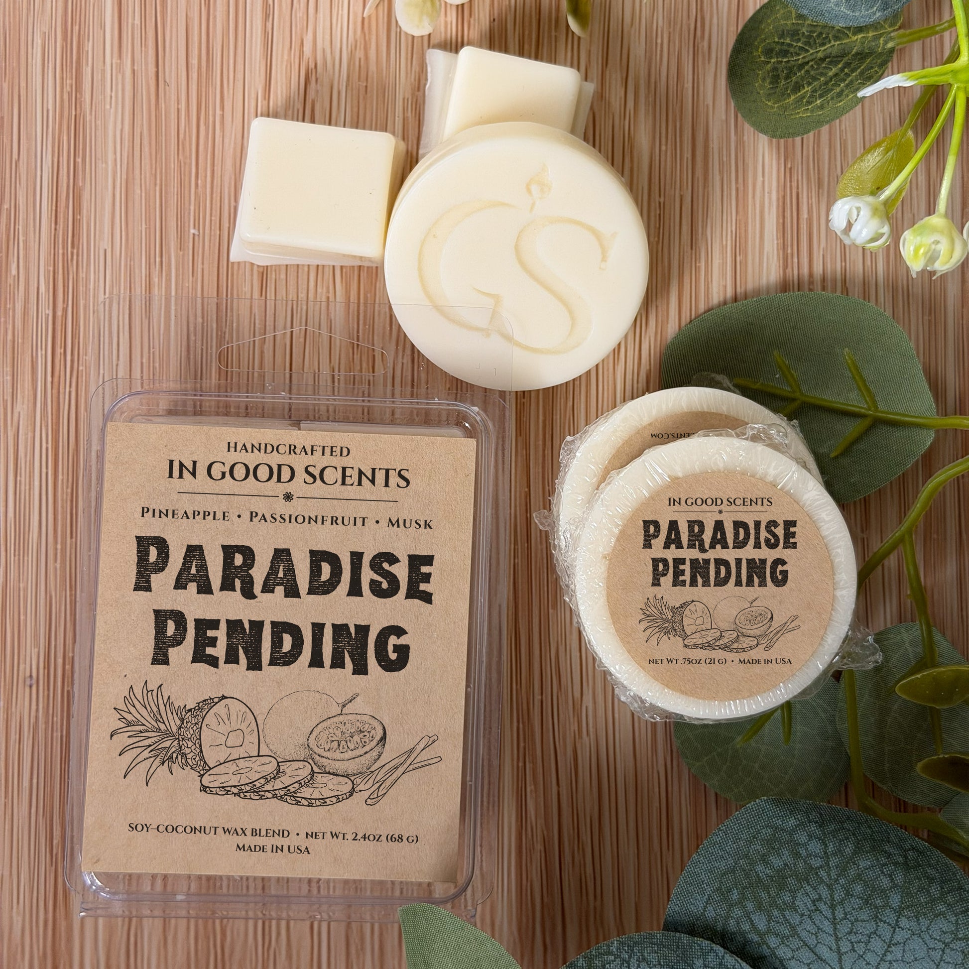 Flat lay of Paradise Pending wax melt clamshell with matching 0.75 oz tart and wax pieces, styled with eucalyptus greenery.