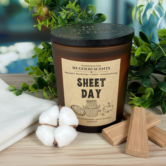 In Good Scents Sheet Day 12oz amber jar candle with black lid on wood surface, cotton stem and wooden wick props.