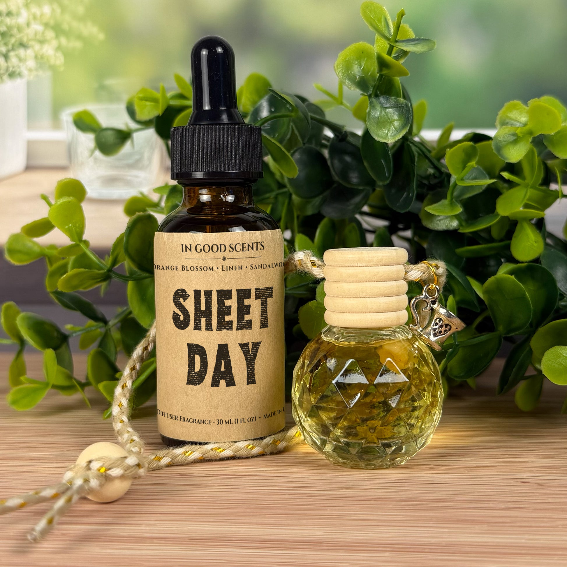 Two small diffuser bottles with labels on a wooden surface with greenery in the background