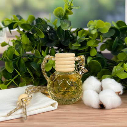 Small glass bottle Diffuser with wooden cap on a wooden surface with green leaves and cotton in the background