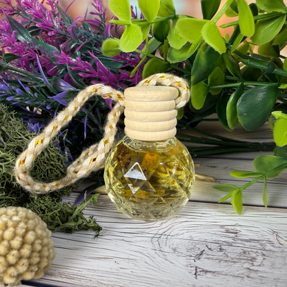 Small bottle diffuser with a rope handle on a wooden surface with plants in the background