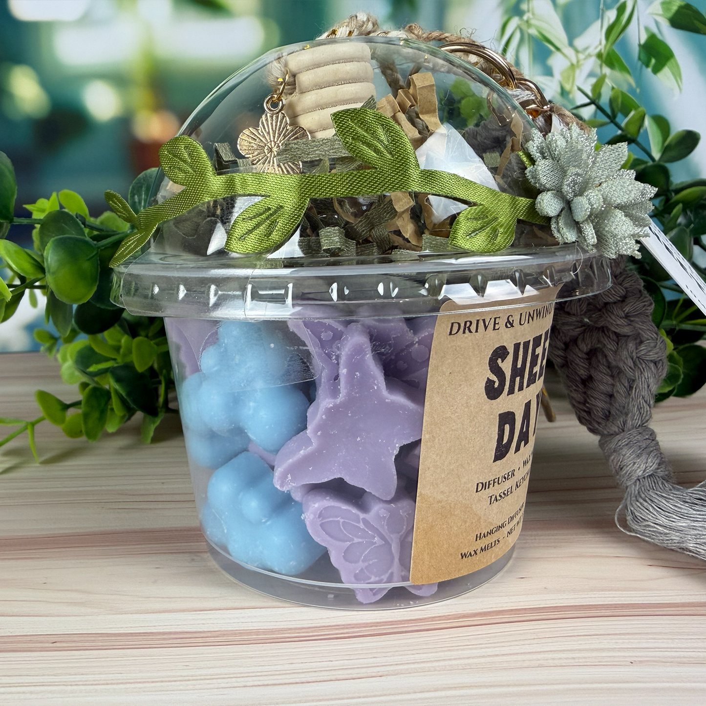 Close-up of Sheet Day Drive & Unwind gift set showing purple and blue wax melts inside a clear cup with decorative ribbon and flower.